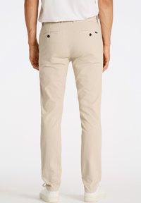 Beige bomuldsbukser med slim fit, der har to baglommer med sorte knapper, og som er parret med hvide sneakers.