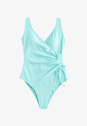 Gros plan d’un maillot de bain texturé turquoise clair avec un côté froncé et un cordon ajustable noué en nœud avec des perles dorées.