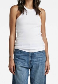 Top tank bianco a costine con scollatura alta, design aderente e senza maniche, abbinato a jeans in denim blu larghi.