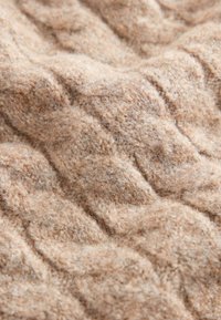 Tissu texturé tricoté en beige doux avec un motif ondulé, affichant une apparence duveteuse et chaude ainsi qu'une qualité tactile délicate.