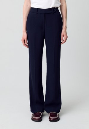 Pantalons larges bleu marine avec une texture lisse, présentant une coupe droite, des plis avant et un détail de bouton sur la ceinture.