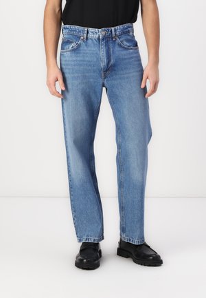 Jean en denim bleu clair avec une coupe droite, comprenant cinq poches, une fermeture à bouton et des coutures contrastées. Se marie bien avec des chaussures noires.