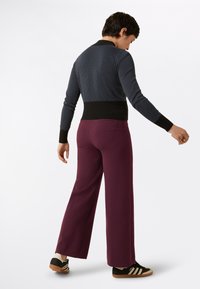 Pullover lavorato a maglia blu scuro con pois bianchi e orlo a coste nero, abbinato a pantaloni larghi bordeaux e sneakers nere con strisce bianche.