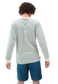Camisa de rayas de manga larga en blanco roto y marino, hecha de una tela suave. Presenta puños de canalé y un ajuste relajado, combinada con pantalones cortos en tonos verde azulado.