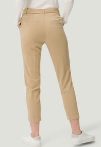 Vue de dos d'une personne portant un pantalon cropped beige, un pull blanc et des baskets blanches, les mains dans les poches.