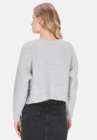 Jasnoszary sweter z dzianiny o skróconym fasonie, szerokimi rękawami i teksturowanej powierzchni. Noszony na czarną spódnicę dżinsową z tylnymi kieszeniami.