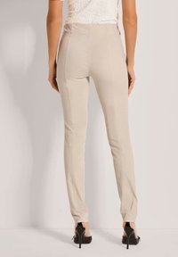 Beige op maat gemaakte broeken van zachte stof, met een hoge taille, slim fit en verticale naden langs de benen.