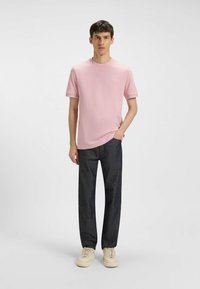 Vaaleanpunainen crew neck -t-paita, jossa on lyhyet hihat, yhdistettynä tummiin farkkuihin ja vaaleankreemisiin tennareihin. Paidassa on hienovarainen logo.