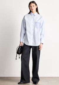 Svetlomodrá košeľa s dlhými rukávmi, zapínaná na gombíky vpredu s náprsným vreckom, kombinovaná s tmavomodrými širokými džínsami s vysokým pásom a malou čiernou taškou.