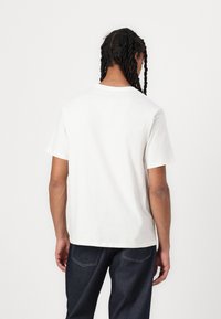 Hvid bomulds-T-shirt med korte ærmer, rund hals og en afslappet pasform. Tekstureret stof med subtile sømdetaljer. Bæres med mørke jeans.