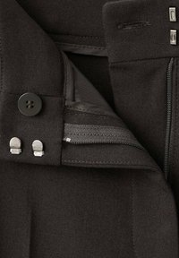 Czarna tkanina tekstylna z kieszenią na zamek błyskawiczny, wyposażona w zapięcie na guzik oraz srebrne elementy ozdobne. Zbliżenie na dopracowane detale projektu.