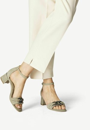 Lichtbeige enkelband sandalen met een korte blokhak, gedragen met crèmekleurige broeken met een zijsplit, wat een stijlvolle outfit benadrukt.