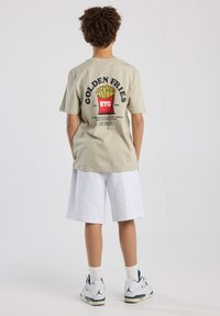 Light beige t-shirt featuring a large graphic of fries and "GOLDEN FRIES NYC" on the back, paired with gray shorts and white sneakers.