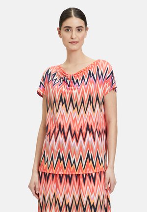 Kurzarmoberteil im lebhaften Zickzackmuster mit Farbtönen von Pink, Orange und Schwarz; weicher, fallender Ausschnitt; leichtes Material.
