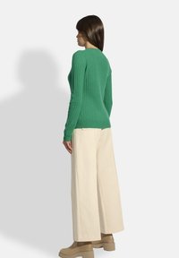 Suéter verde de punto acanalado con mangas largas, cuello redondo, combinado con pantalones beige holgados y botas beige gruesas. Diseño simple y texturizado.