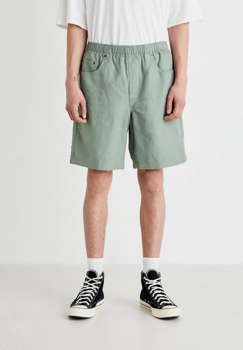 Pantaloni scurți de culoare verde deschis, până la genunchi, confecționați dintr-un material texturat. Au o talie elastică, două buzunare laterale și o croială lejeră.