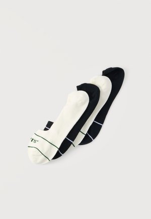 Quatre chaussettes basses alternant noir et blanc, deux avec de fines rayures colorées près des orteils sur un fond clair uni.