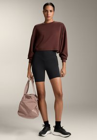 Brown cropped sweatshirt, black high-waist shorts, and black sneakers. Light pink bag with shoulder straps. Smooth fabric, relaxed fit.