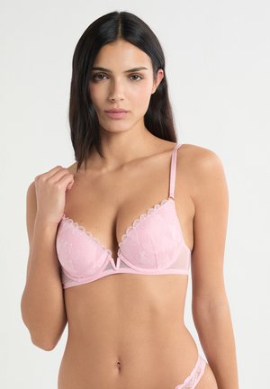 Rosa Spitzen-BH mit einem wellenförmigen Rand, dreieckigen Cups und dünnen verstellbaren Trägern. Ein zartes Herzmuster verziert den Stoff.