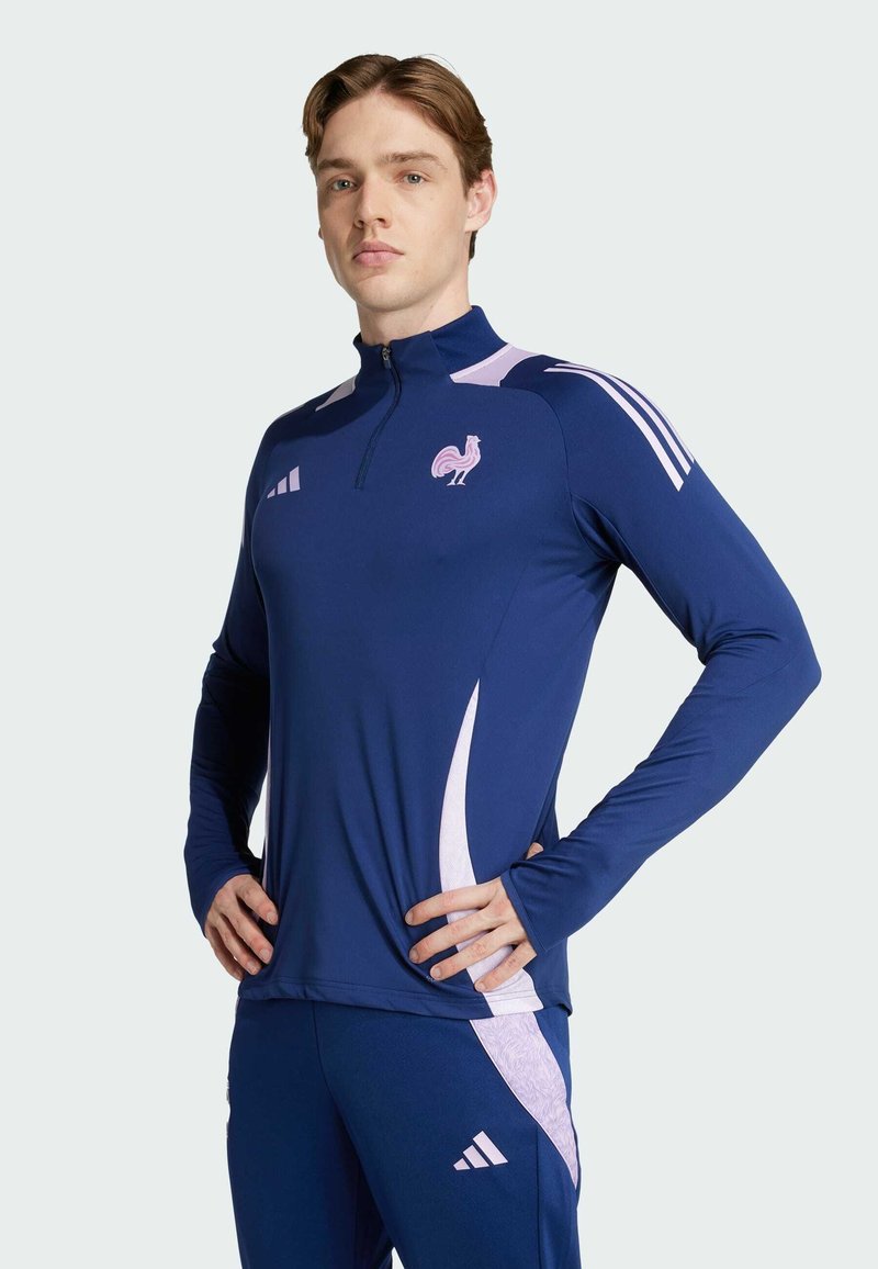 Mornarica sportska majica dugih rukava s četvrtim patentnim zatvaračem, ružičastim detaljima i logotipom pijetla. Izrađena je od glatkog materijala s prikladnim dizajnom.