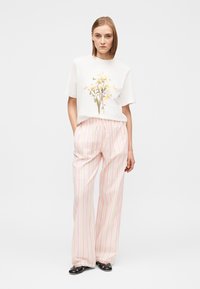 Λευκή μπλούζα με λουλουδάτο σχέδιο, συνδυασμένη με ροζ ανοιχτό ριγέ παντελόνι με φαρδιές παντελόνες, που διαθέτει ελαστική μέση και δαντέλα στο τελείωμα.
