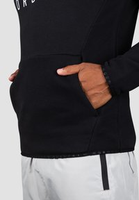 Felpa nera con tasca a marsupio, tessuto testurizzato e cuciture visibili. Presenta un logo stampato sul petto e dettagli a contrasto sull'orlo.