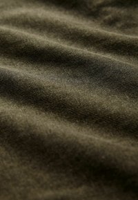 Tessuto verde oliva scuro con una superficie texturizzata, caratterizzato da schemi di tessitura visibili e da una leggera lucentezza, disteso in morbide pieghe ondulate.