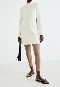 Robe pull côtelée crème, manches longues, fentes sur les côtés. Portée avec des leggings beiges et des ballerines imprimé léopard avec des accents de lanières.