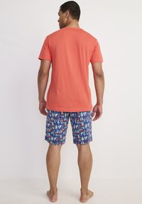 Korallfärgad t-shirt med kort ärm som kombineras med blå mönstrade badshorts med färgglada segelbåtar. Avslappnat, lättviktsmaterial.