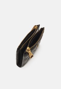 Portafoglio in pelle trapuntata nera con zip in oro e un'etichetta. Ha due scomparti e una superficie liscia, progettato per l'organizzazione.