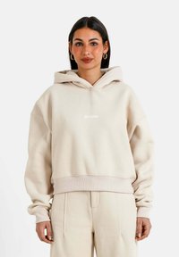 Hoodie oversize beige con una tasca a marsupio e polsini a costine, con un piccolo logo bianco sul petto. Tessuto morbido e texturizzato.