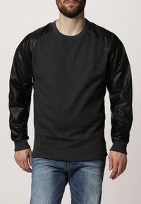 Sudadera gris oscuro con mangas raglán de imitación cuero negro. Puños y dobladillo acanalados, cuello redondo, tejido texturizado, corte casual.