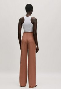 Wijde broek in een warme terracotta kleur, gemaakt van zachte stof met een elastische tailleband. Gepaard met een strakke witte tanktop.