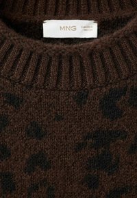 Rjava pletena jopica z črnimi leopardjimi madeži in belo oznako velikosti, ki bere MNG, EUR USA S, MEX CH na rebrastem ovratniku.