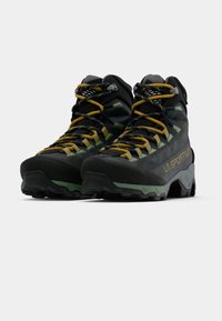 Melnas un zaļas pārgājienu zābaki ar teksturētu apdari. Iekļauj dzeltenus auklas, mīkstu apkakli un izturīgu zoli labākai saķerei.