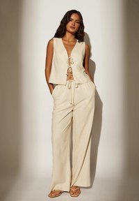 Top court en lin beige avec un col en V et un détail noué à l'avant, associé à un pantalon large avec un cordon de serrage ajustable et des poches latérales.