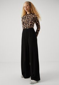 Leopard print long-sleeve top paired with high-waisted black wide-leg trousers. Model wears silver sneakers with color accents. Soft fabric textures.