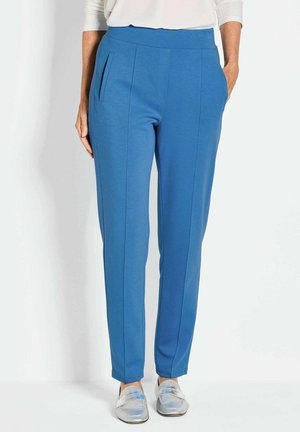Blauwe op maat gemaakte broek met een gladde textuur, voorzien van zijzakken, verticale naden en een brede tailleband. Gepaard met glanzende zilveren schoenen.