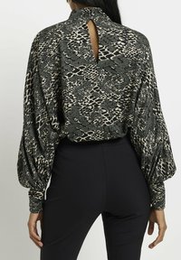 Blouse à manches longues ornée d'un imprimé serpent noir et beige, col haut, découpe en forme de clé au dos et manches bouffantes volumineuses.