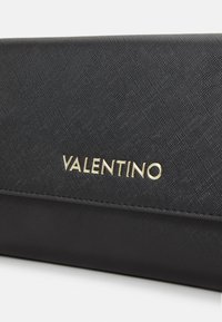 Pochette en cuir noir avec une finition texturée, arborant un logo doré "VALENTINO" bien en vue à l'avant.