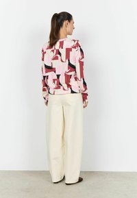Langærmet top med et flerfarvet abstrakt mønster i pink, sort og rød; kombineret med cremegule bukser med vide ben.