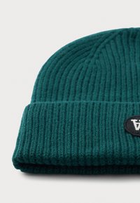 Beanie a coste di colore verde scuro con risvolto e toppa circolare nera con un logo "A" stilizzato bianco su sfondo bianco.