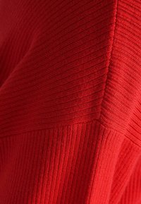 Czerwony dzianinowy sweter prążkowany z teksturowanym wykończeniem, z ukośnym szwem i różną szerokością prążków, tworzącymi strukturalny wygląd.