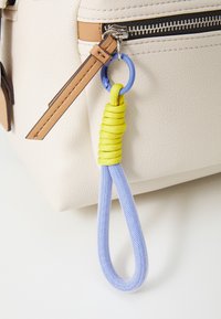 Fargerik nøkkelring med en blå løkke og en spiralformet gul detalj, festet til en beige bag med lærdetaljer og glidelås.