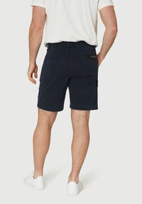 Chino bleu marine en mélange de coton, avec des poches latérales et arrière, un ourlet cousu et un détail de label noir sur la ceinture.