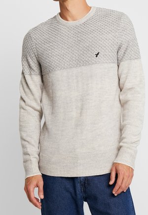 Maglione grigio chiaro a maglia con un motivo a diamante testurizzato sulle spalle e polsini e orlo a costine. Presenta un sottile accento con logo.
