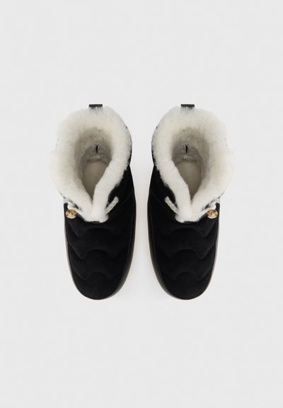 Botas de tobillo de ante negro con un forro de piel sintética blanca, textura ondulada en la parte superior y cordón decorativo con un acento de bead de madera en el cuello.