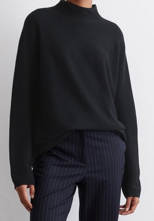 Black long-sleeve sweater with a high neckline, made from a soft texture, paired with navy pinstripe trousers.