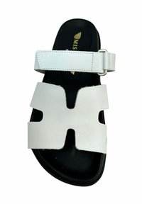 Sandalia de cuero blanca con punta abierta, que presenta un gran diseño recortado y una correa ajustable en el tobillo. Suela negra con detalle de marca.