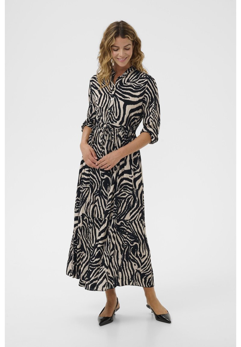 Lång, knäppt klänning i zebramönster, med neutrala nyanser av beige och svart, och en bältesmidja samt volangkjol. Svarta skor.